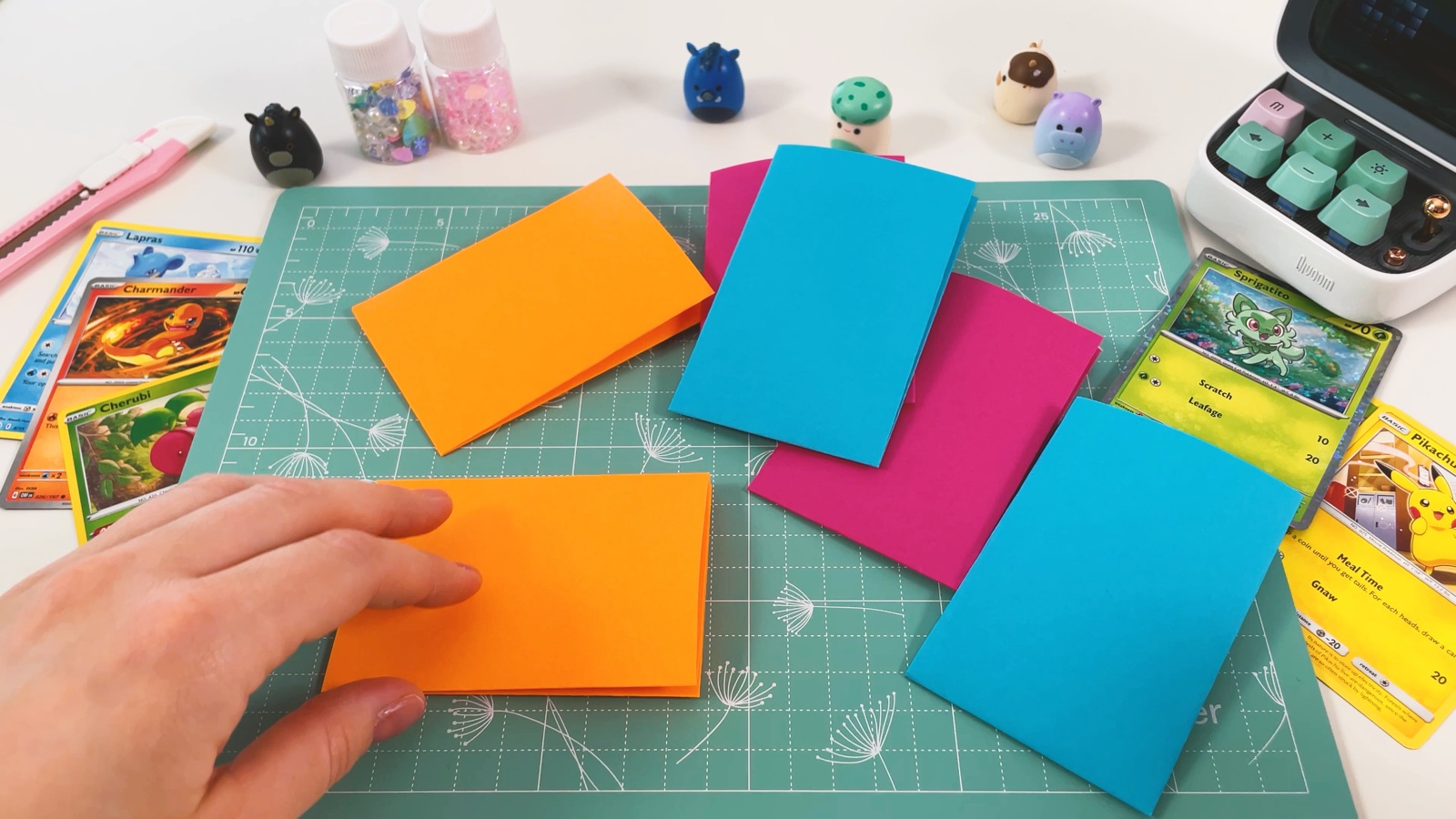 Gefaltete Fächerteile in Orange, Blau und Rosa liegen auf der Schneidematte