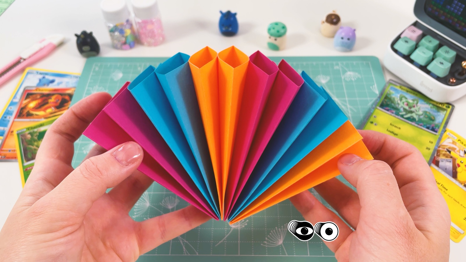 Die geklebten Fächer, geöffnet zu einem Regenbogen aus orangem, rosa und blauem Papier