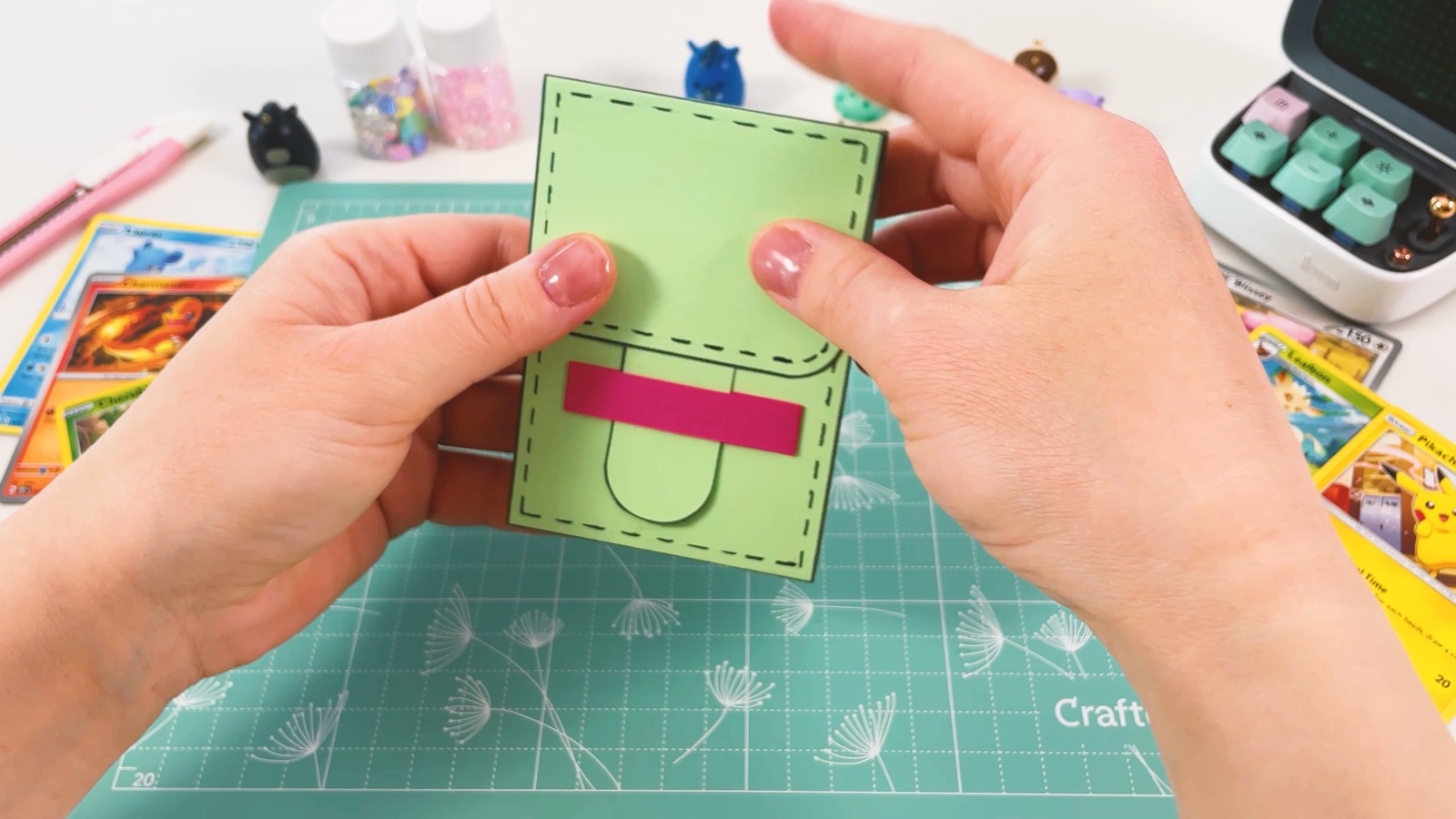 Das rosa Band ist quer über die Vorderseite der Hülle geklebt, die grüne Lasche steckt darunter
