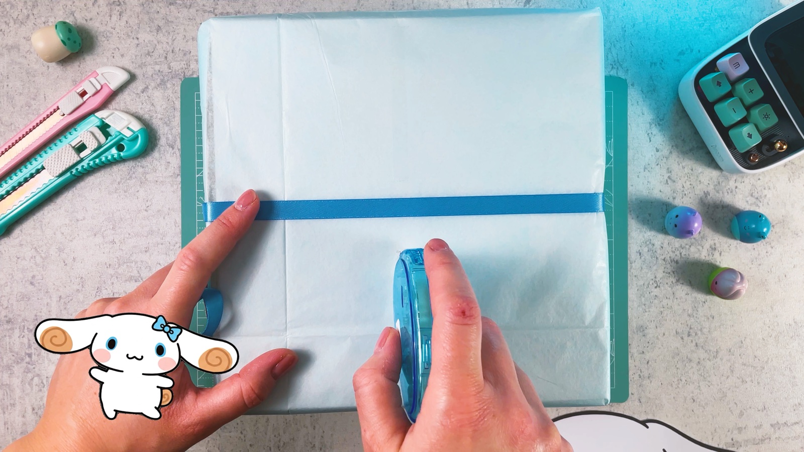 Se presiona un listón azul sobre la caja azul claro mientras se fija con cinta