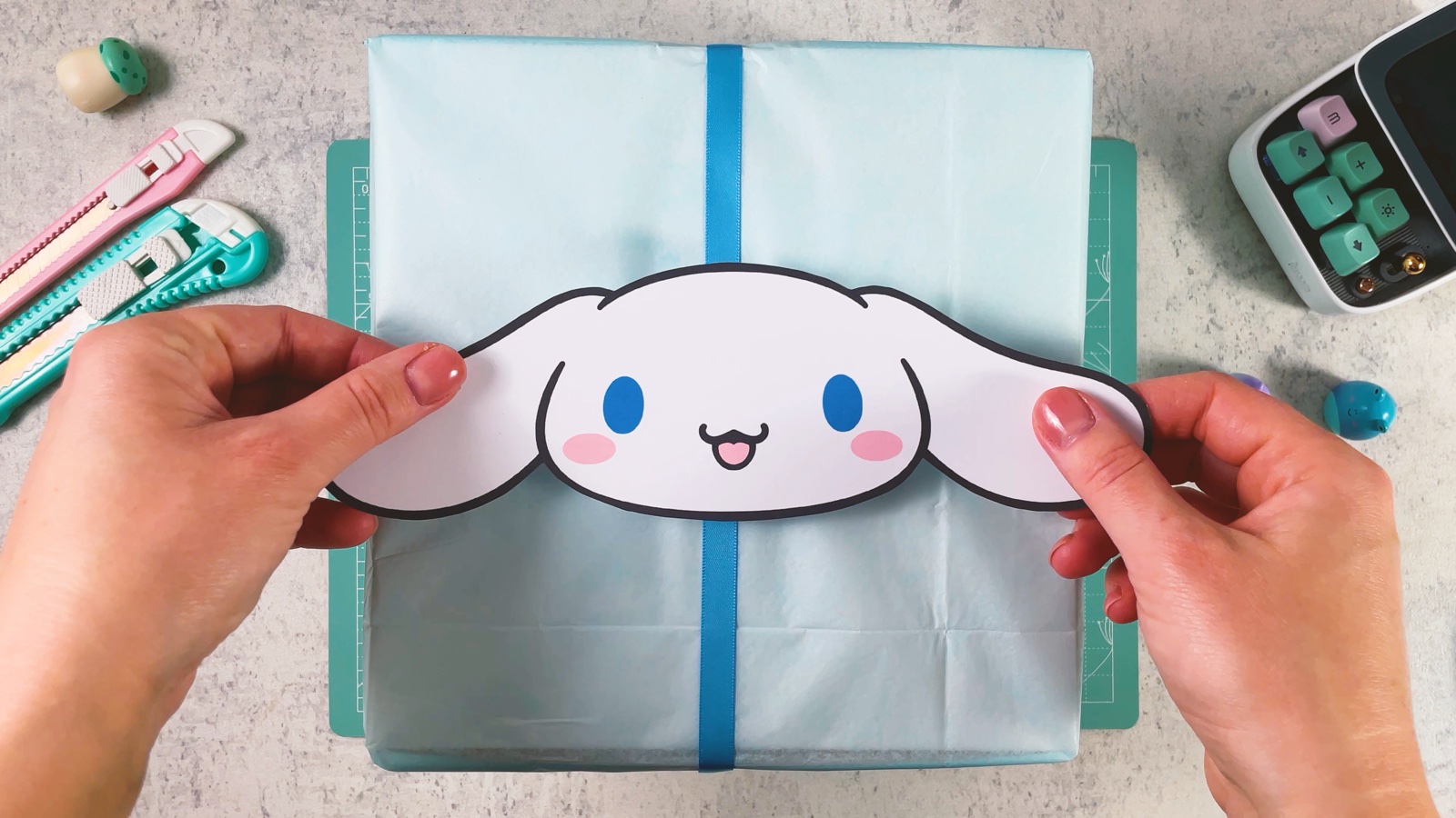Se coloca la carita de Cinnamoroll sobre el cruce de listones de la caja