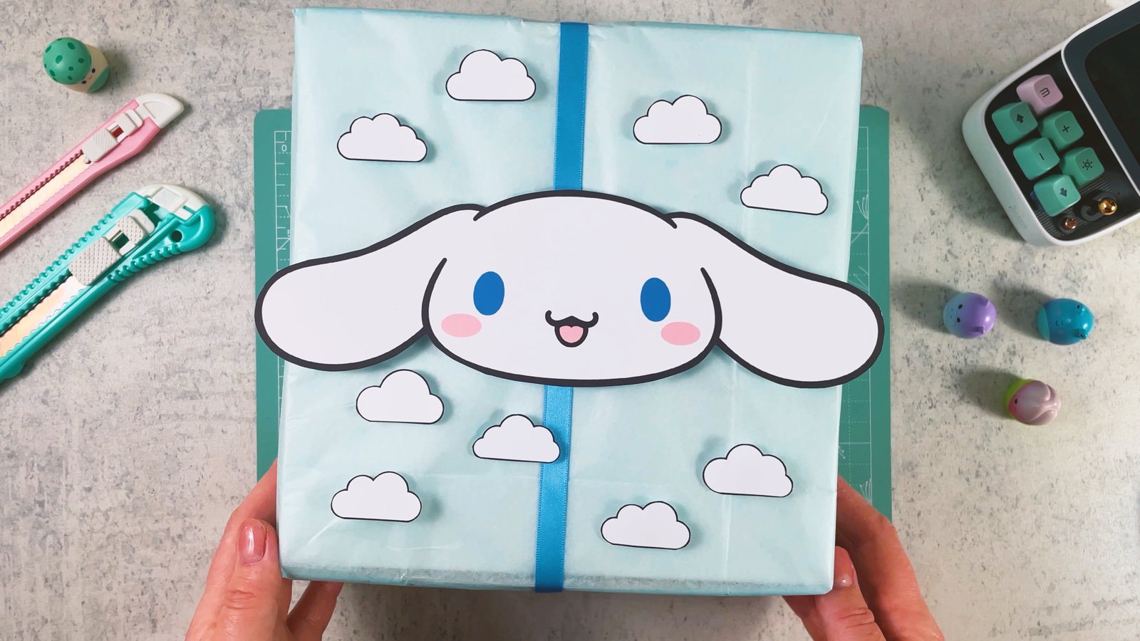 El regalo de Cinnamoroll terminado: caja azul claro, cruce de listón azul, una gran carita blanca y nubes