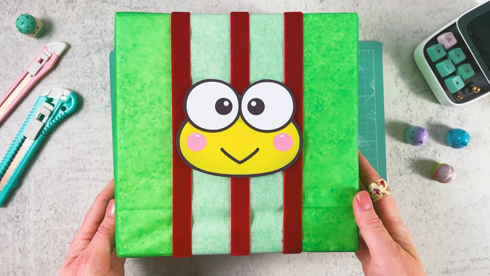 El regalo de Keroppi terminado: caja verde con rayas verde pálido y rojo oscuro y una gran cara de rana