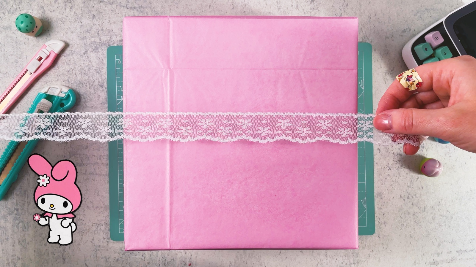 Se coloca un listón de encaje blanco sobre una caja envuelta en papel de regalo rosa
