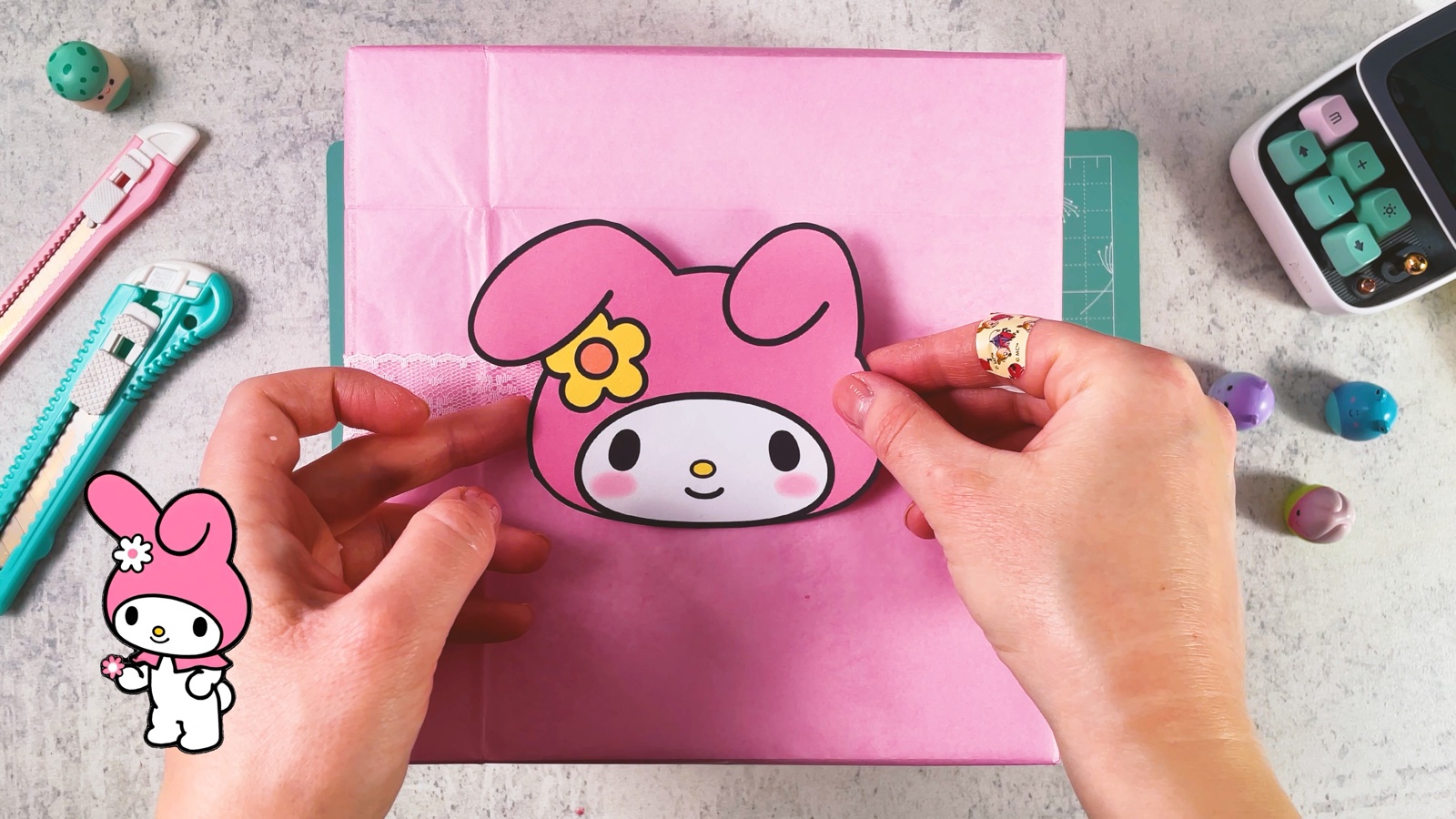Se presiona la carita de My Melody sobre la caja rosa, arriba del listón de encaje
