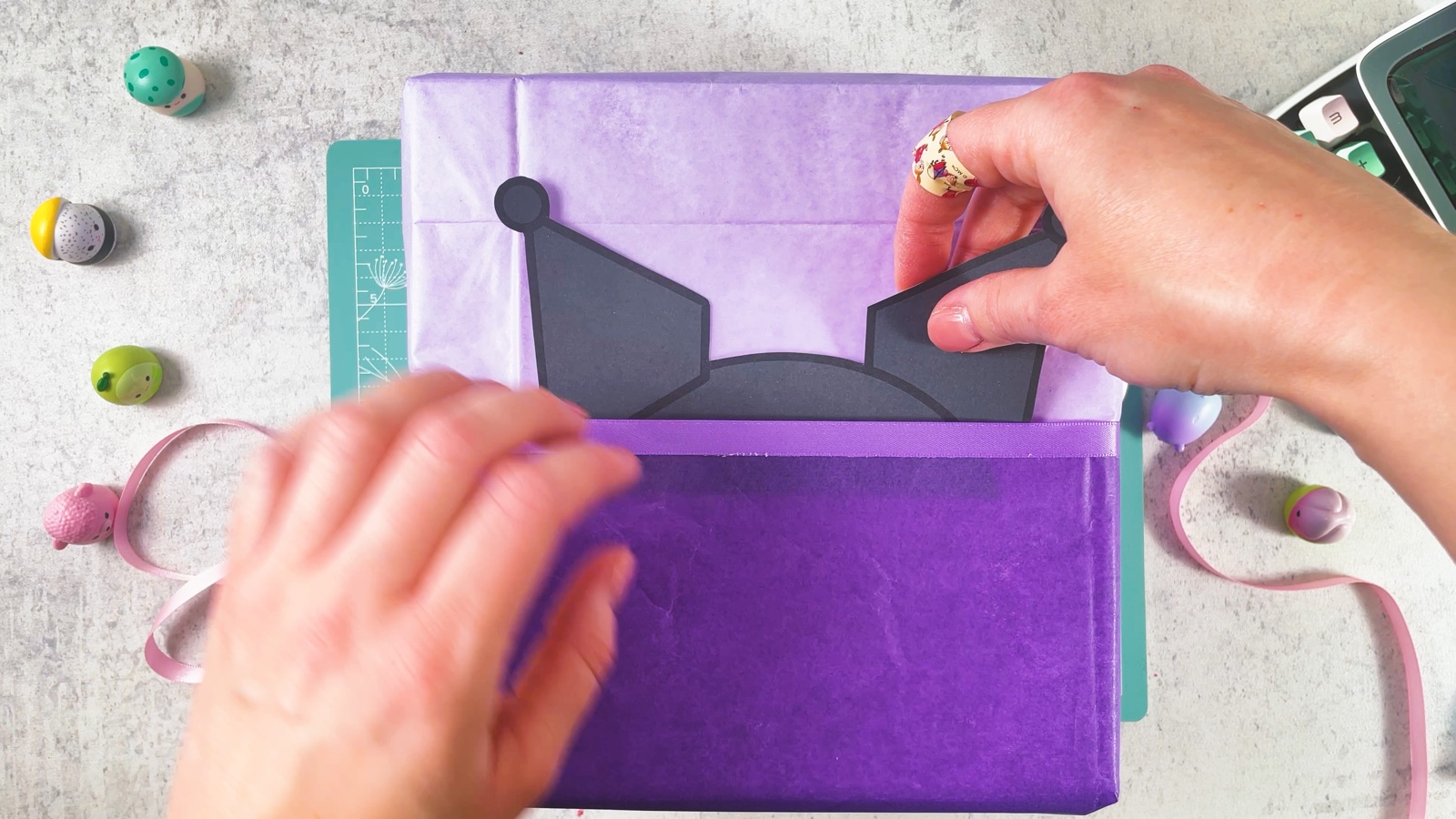 Se mete la figura de la capucha negra de Kuromi detrás del papel morado oscuro