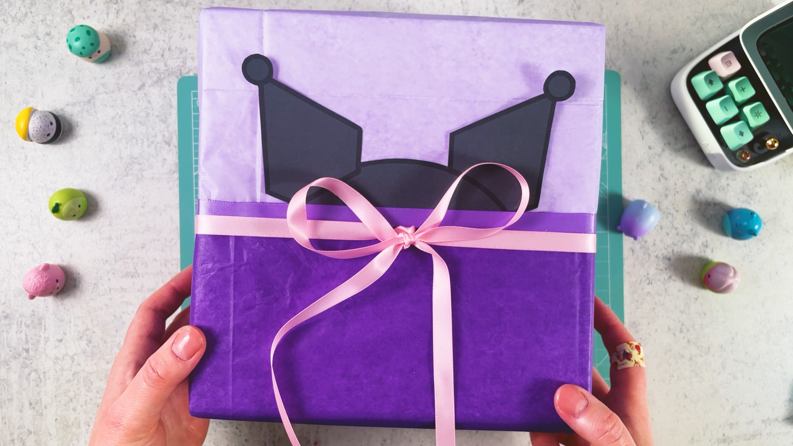 El regalo de Kuromi terminado: caja lila y morado oscuro con orejas negras y un moño rosa