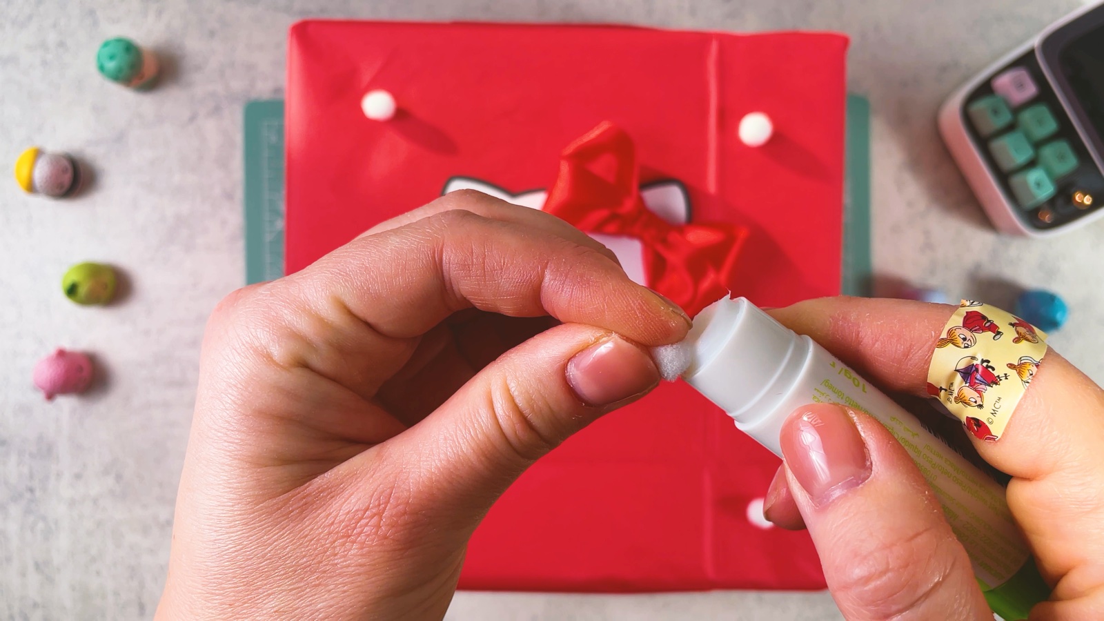 Se ponen toques de pegamento en la caja roja para pegar pompones blancos pequeños