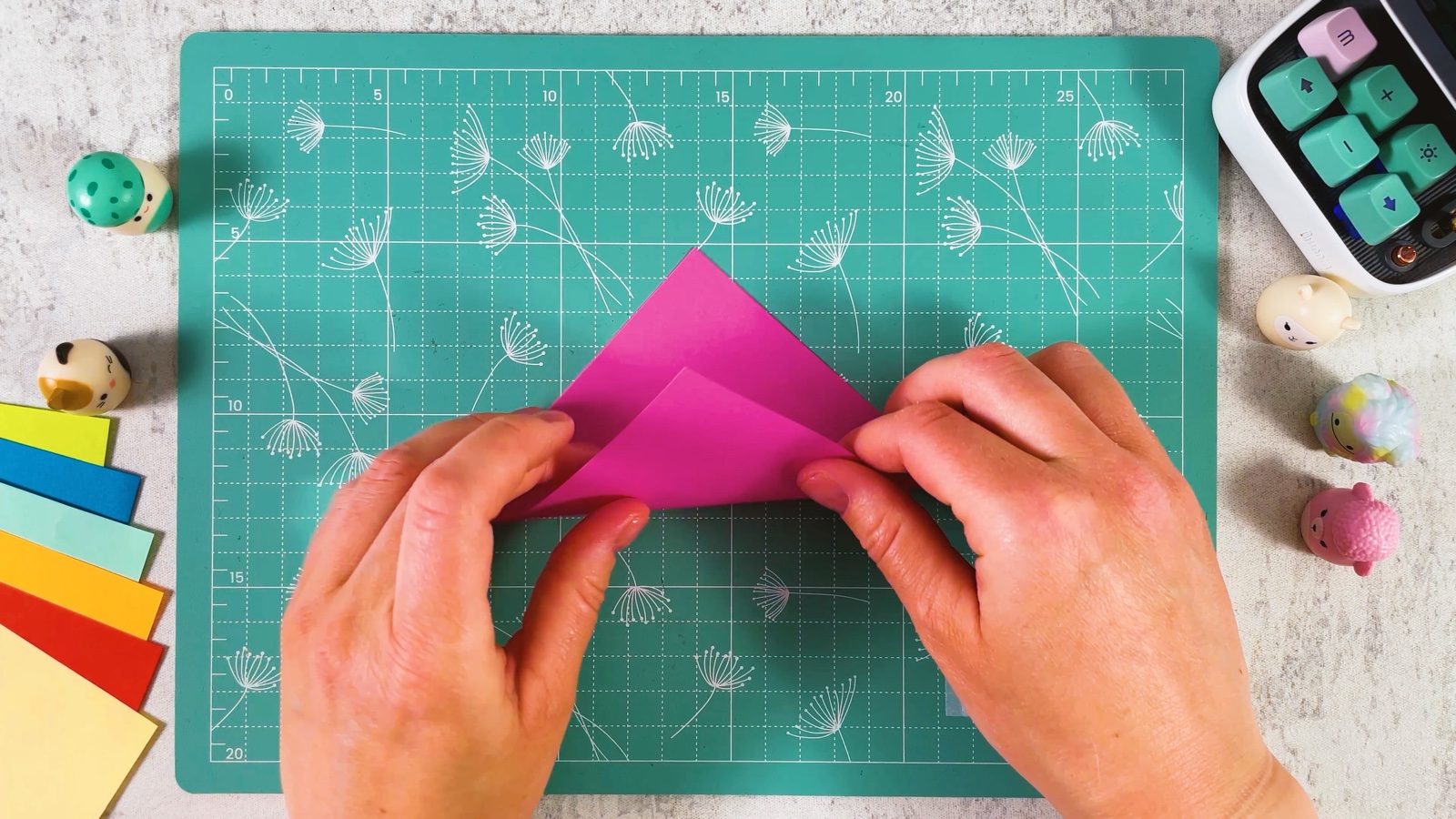 Folding the pink square in half from corner to corner into a triangle