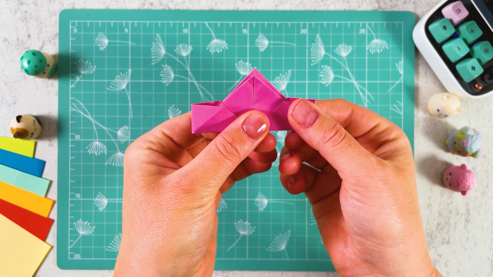 Pushing the sides of the folded pink square inwards so it rises into a point with two flat wings