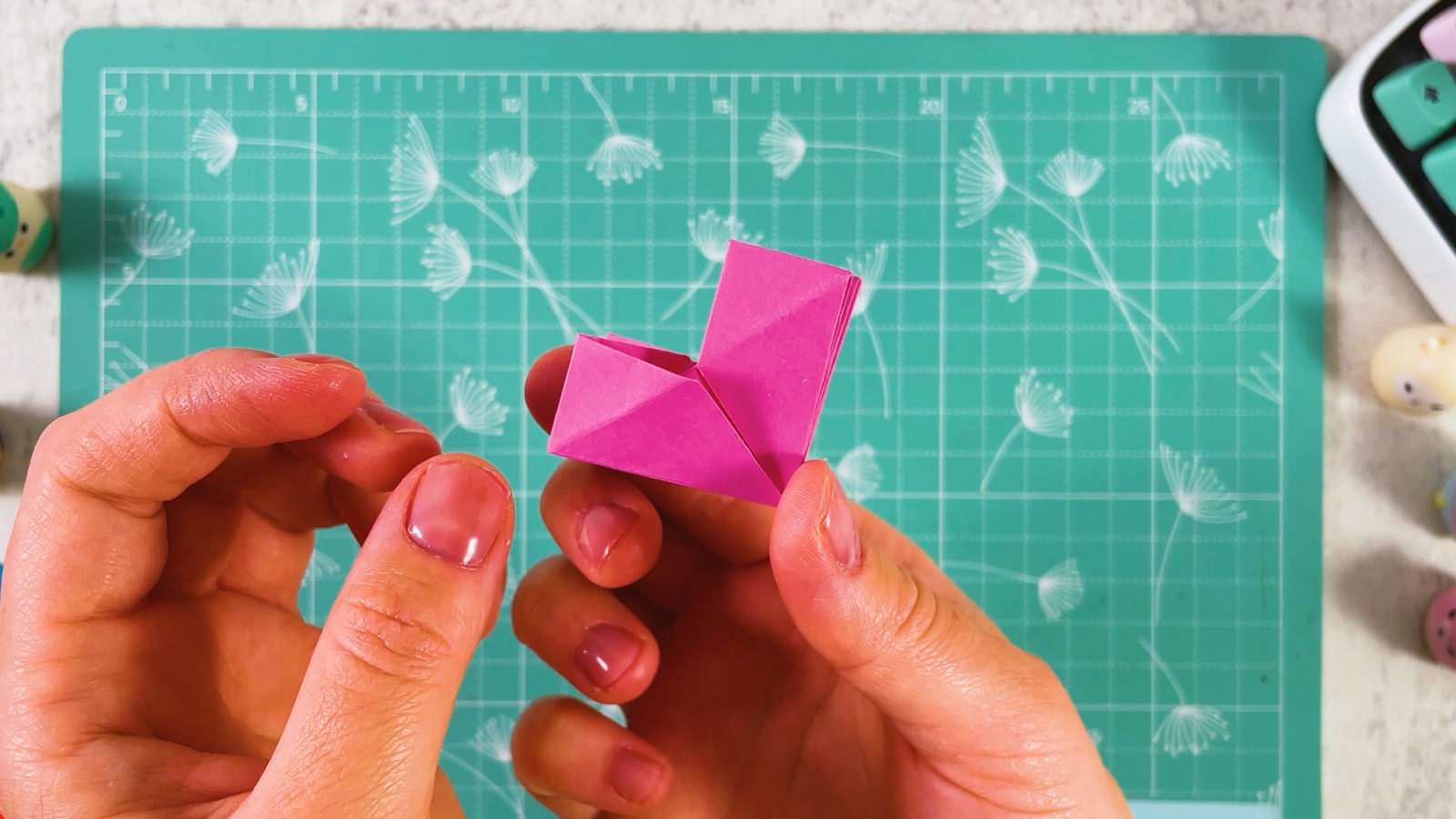 The finished pink piece held up in one hand, folded into a small heart-shaped V