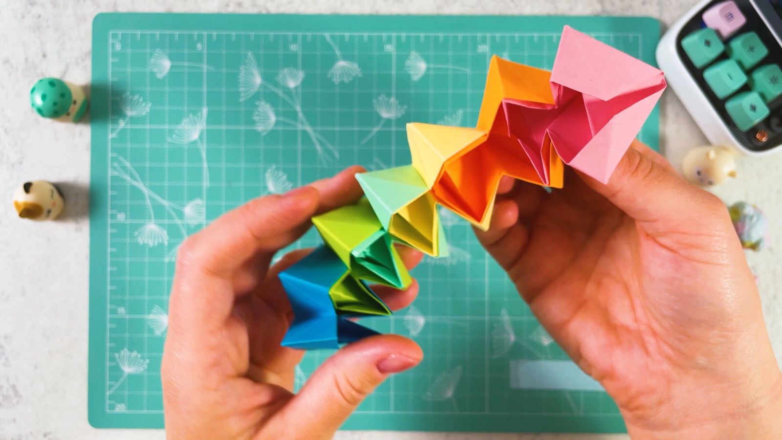 A long zigzag chain of joined paper pieces in rainbow colours, held in both hands