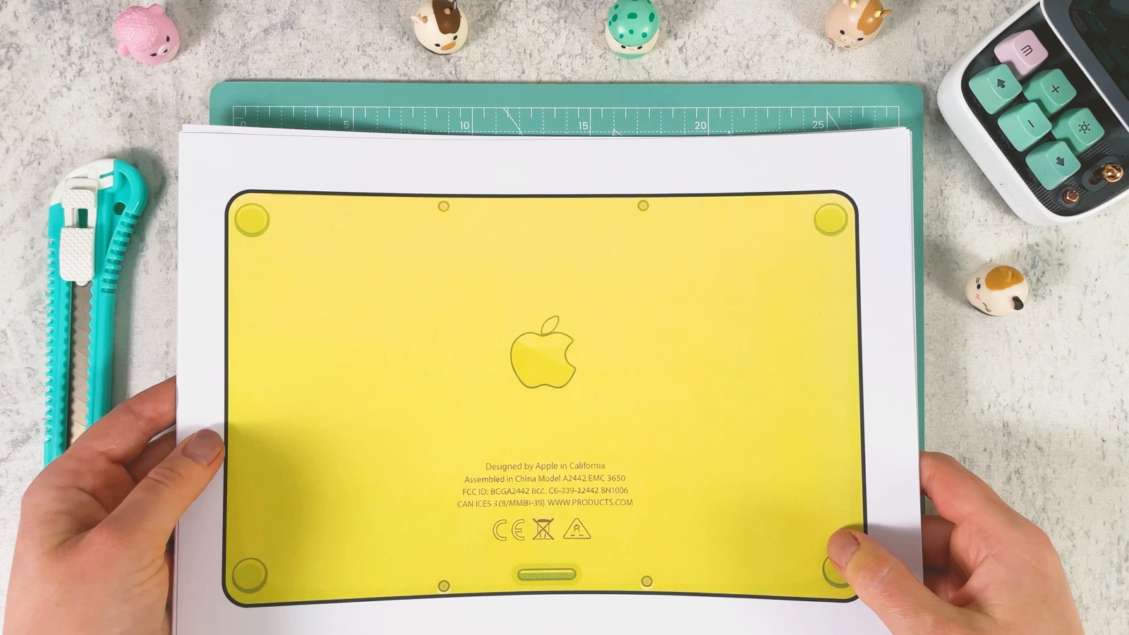 Die ausgedruckte Unterseite des Laptops, ein gelbes Rechteck mit runden Ecken und dem Apple-Logo, auf der Schneidematte