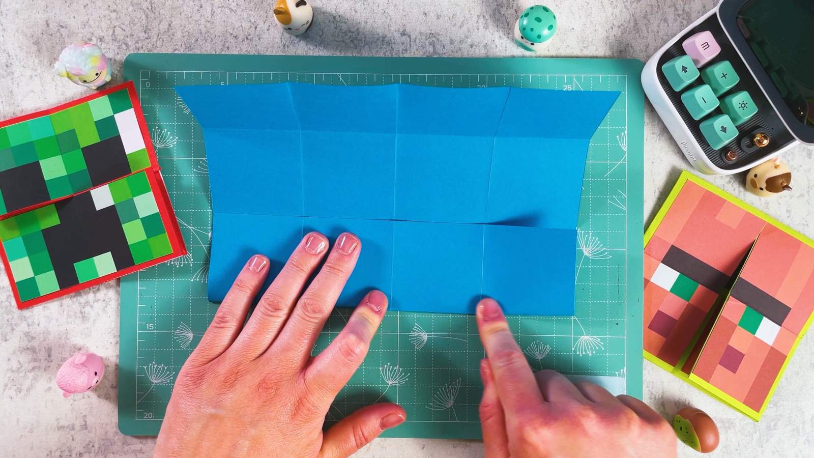 Folding the edges of the blue paper to the middle in the other direction, with the first creases visible