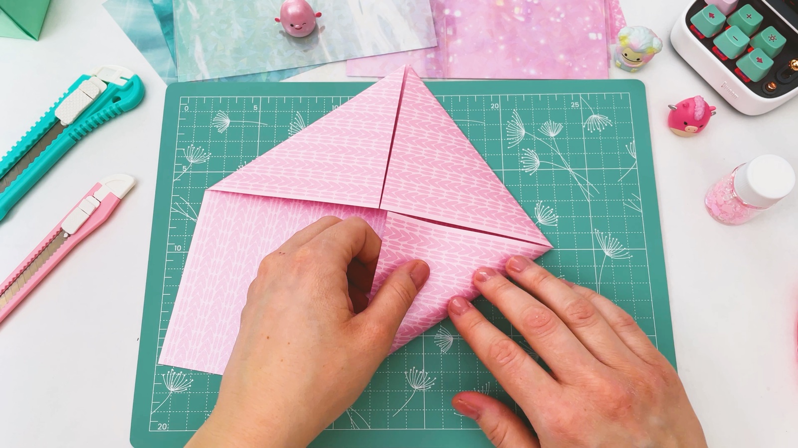 Das rosa Quadrat wird von Ecke zu Ecke zu einem Dreieck gefaltet, so entsteht eine diagonale Falte