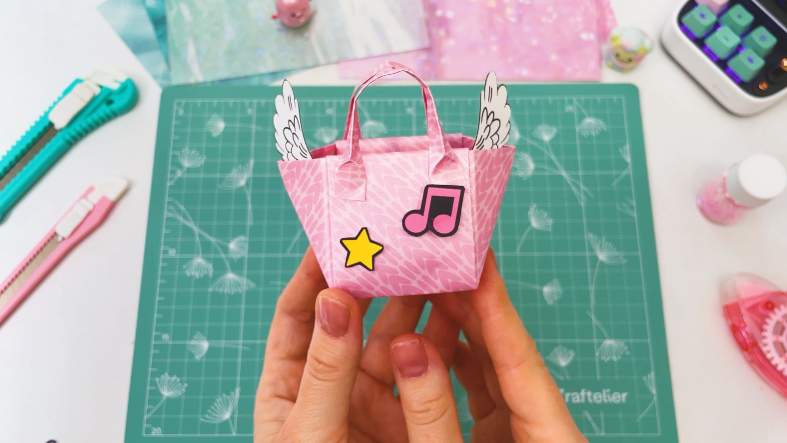 Die fertige hellrosa Papiertasche mit zwei Henkeln, weißen Papierflügeln an beiden Seiten, einem gelben Stern und einer rosa Musiknote