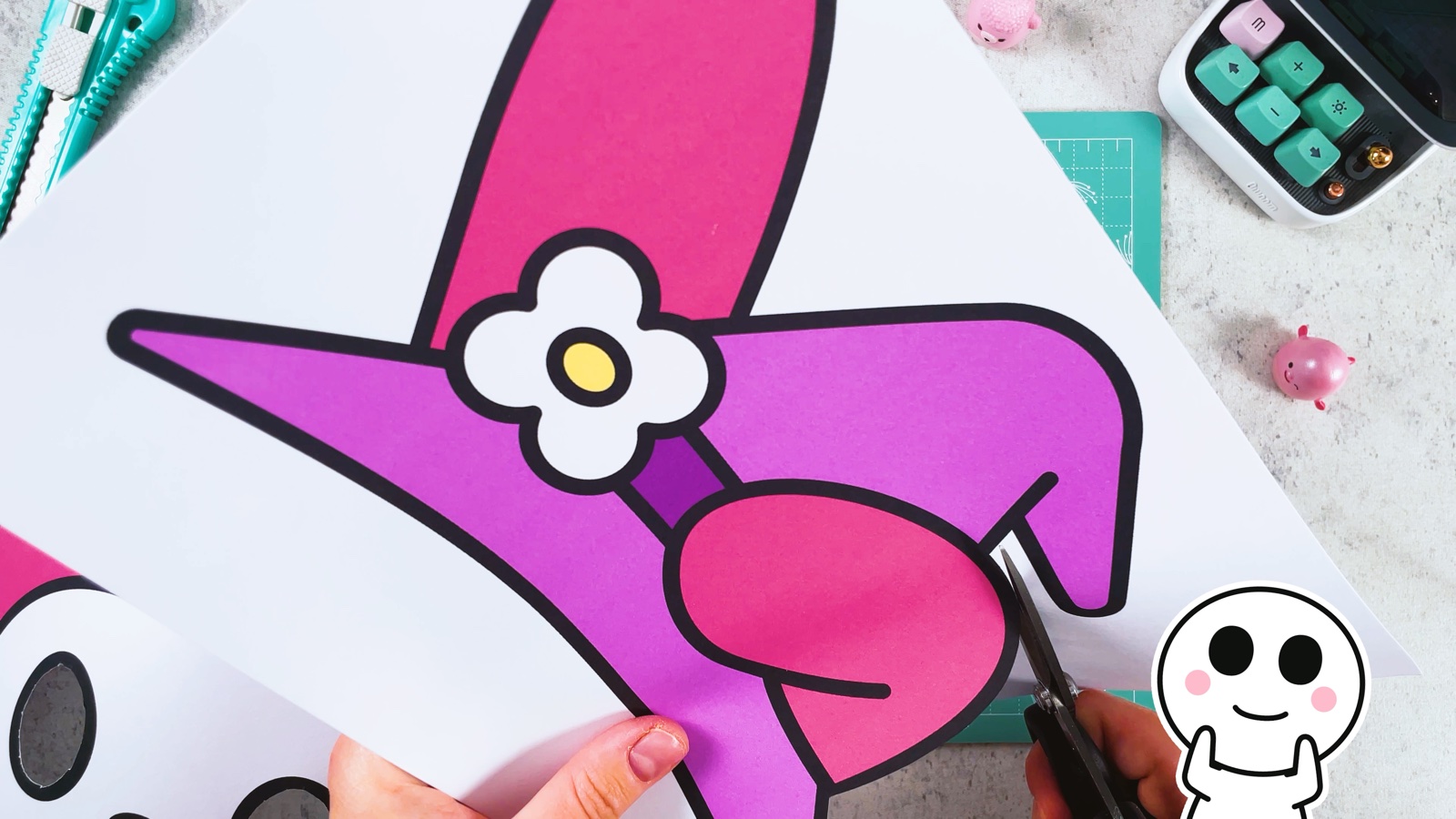 Um den lila Hexenhut mit der weißen Blume und der rosa Schleife wird herumgeschnitten