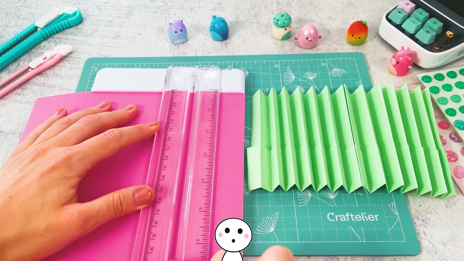 Une longue bande de papier rose coupée avec un massicot, à côté de l’accordéon vert