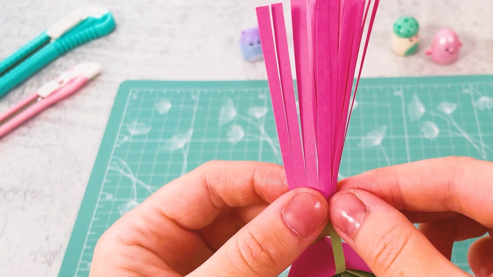 Le pompon rose roulé, pincé fort en haut pour que la colle tienne, juste au-dessus de l’éventail