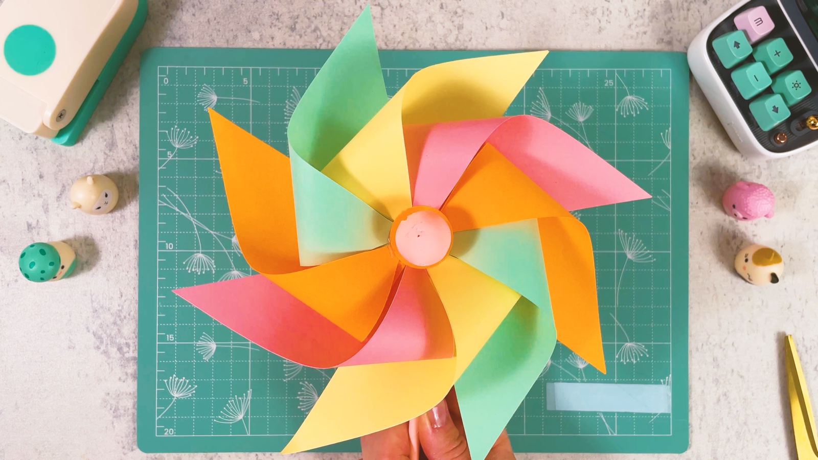 Das fertige Windrad aus Papier mit acht gebogenen Flügeln in Orange, Rosa, Gelb und Mint und einer rosa Kugel in der Mitte