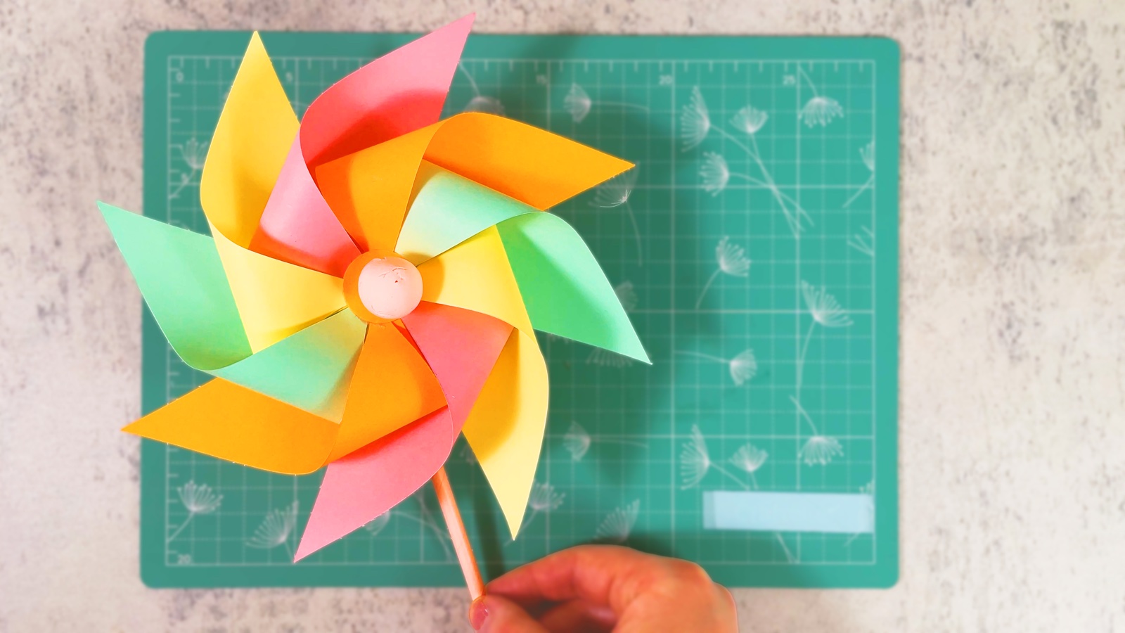A finished paper pinwheel with orange, pink, yellow and mint blades