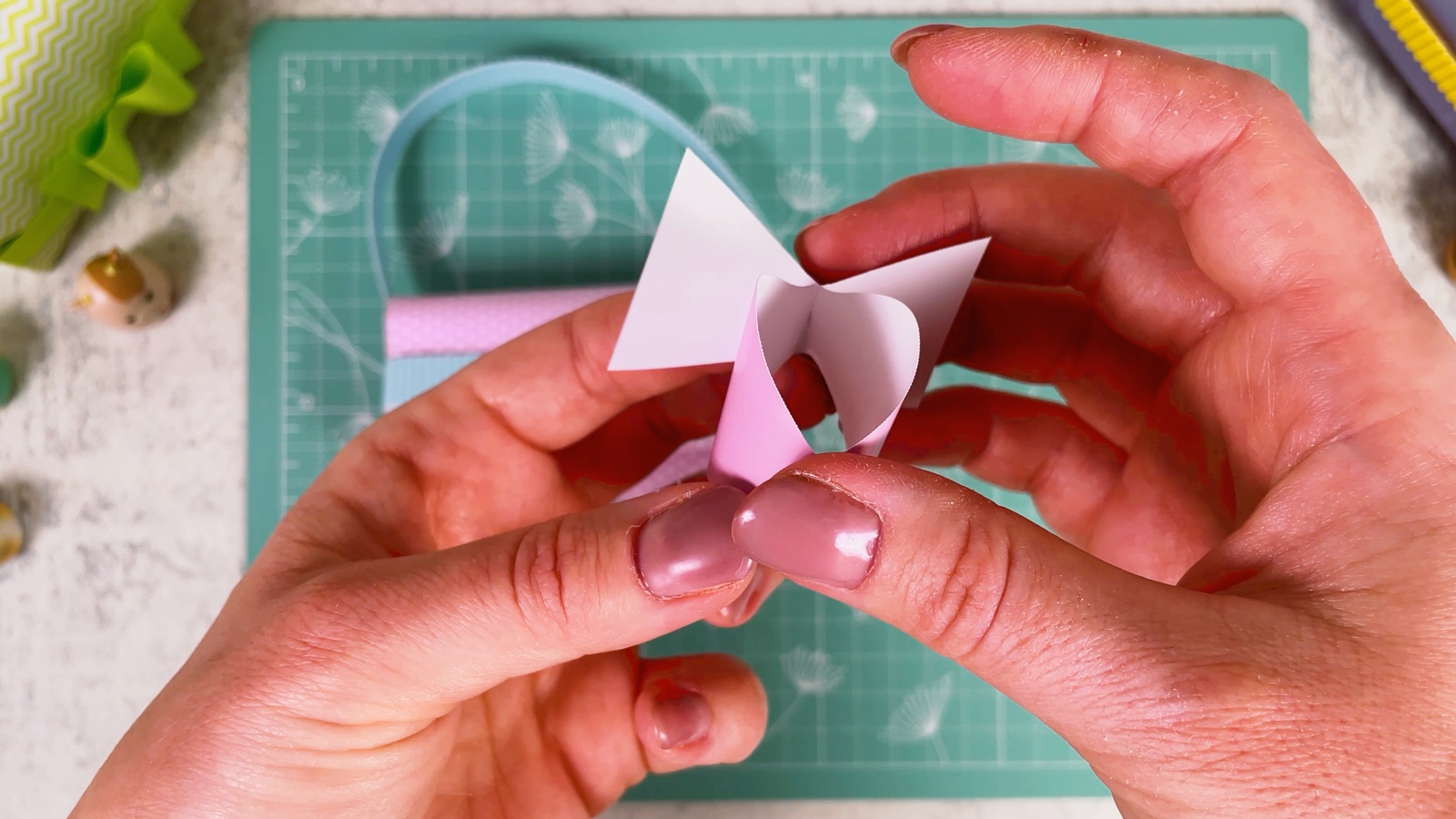 Folding the ends of the pink paper into the loops of a bow
