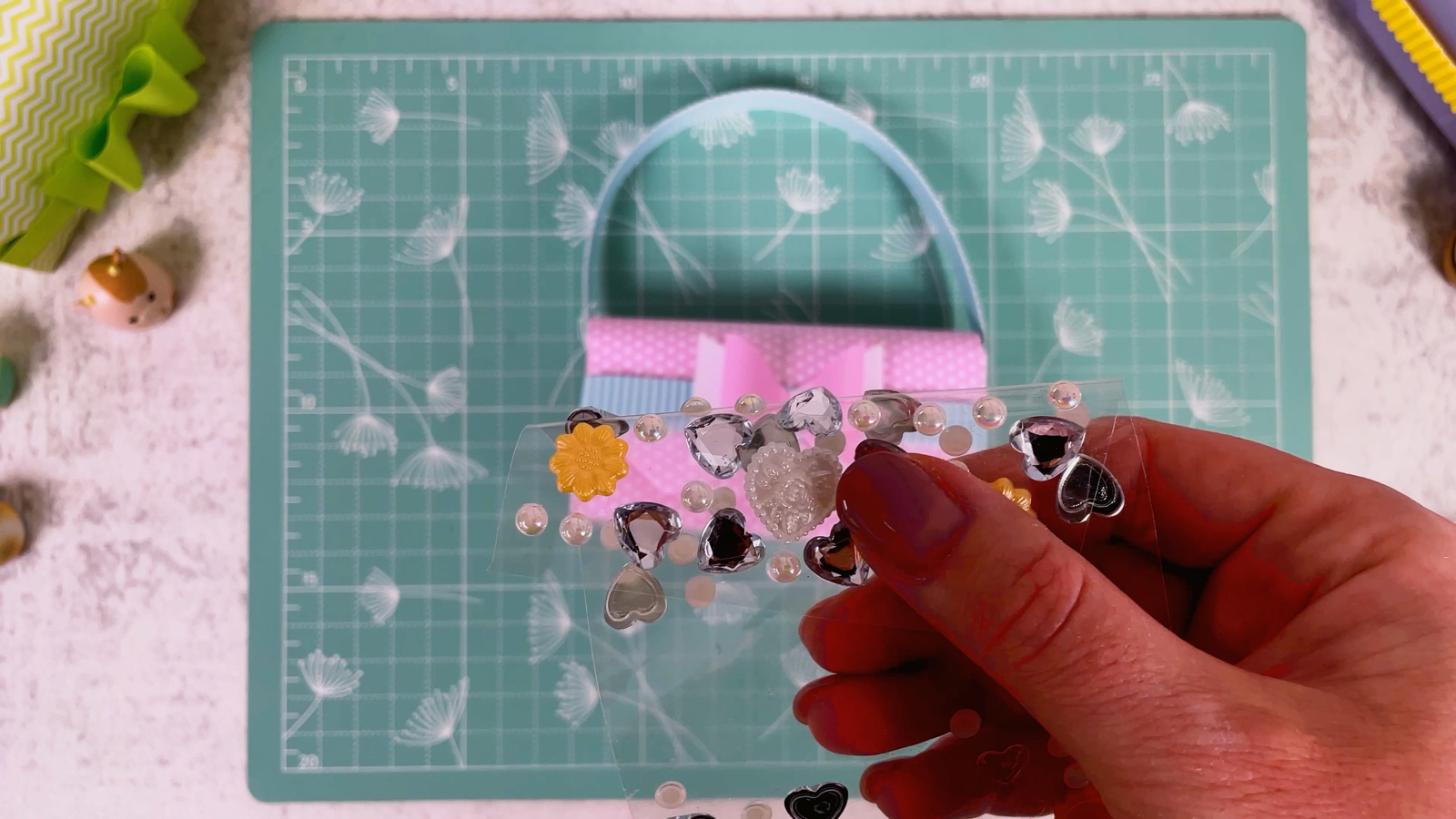A sheet of heart gems, crystals and pearl stickers held next to the purse with the bow