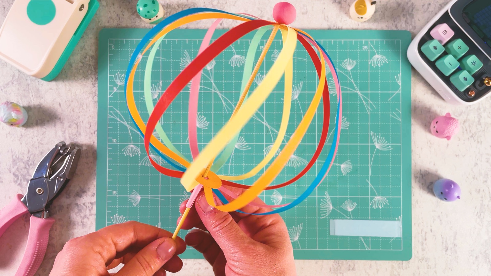 El juguete de papel terminado como una bola redonda de colores del arcoíris en un palito de brocheta, con una bolita de plastilina rosa arriba