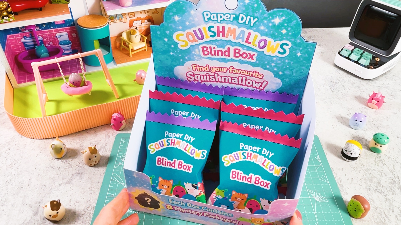 Bolsas sorpresa con bordes en zigzag rosas y morados, en fila dentro de una caja exhibidora de papel