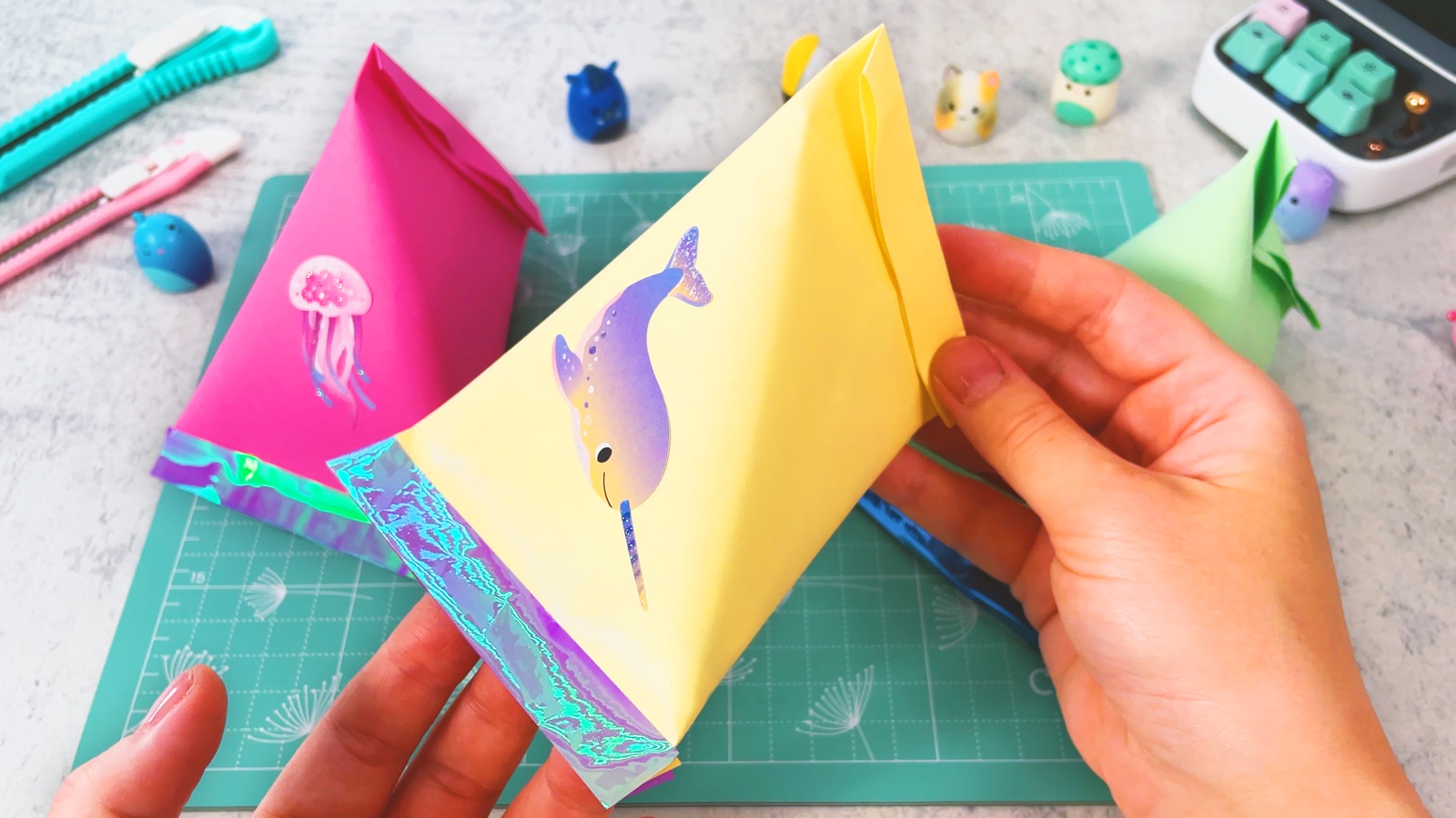 Finished paper party favour bags with a jellyfish and a narwhal, holographic bottom edges, on a mint cutting mat
