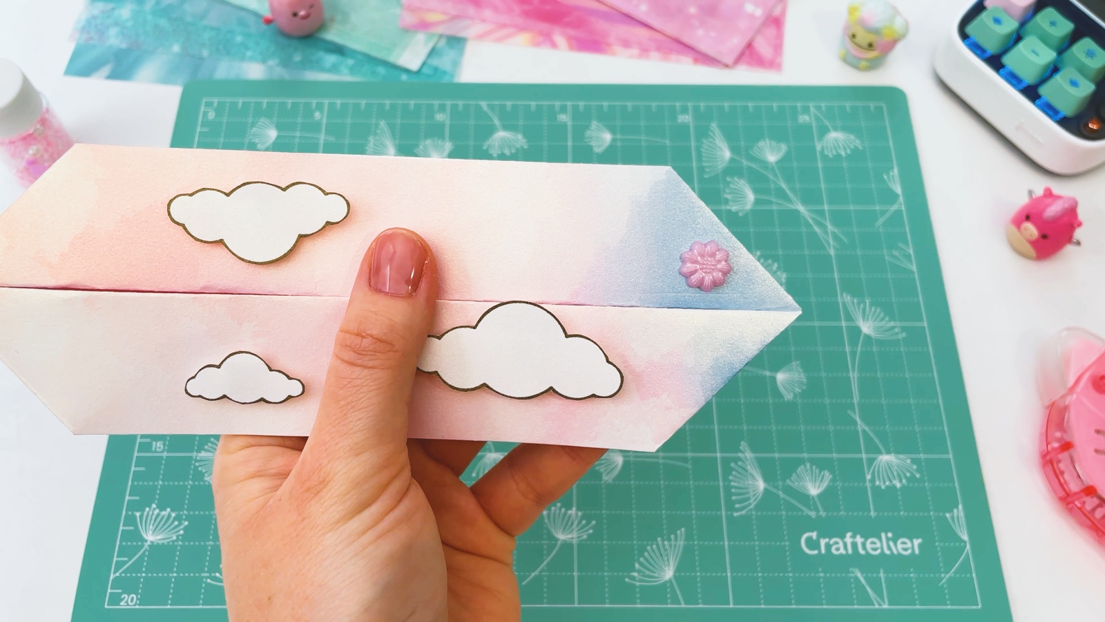 The closed pencil case with clouds on both halves and a pink flower gem at the end