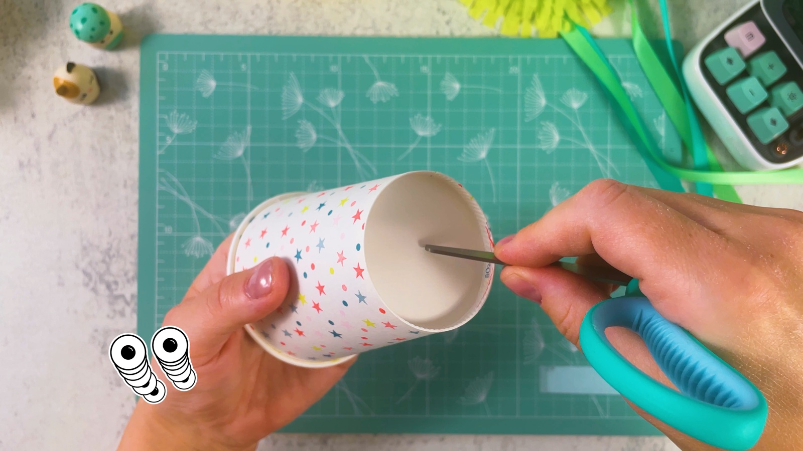 Poking a small hole in the bottom of a star-patterned paper cup with the tip of the scissors