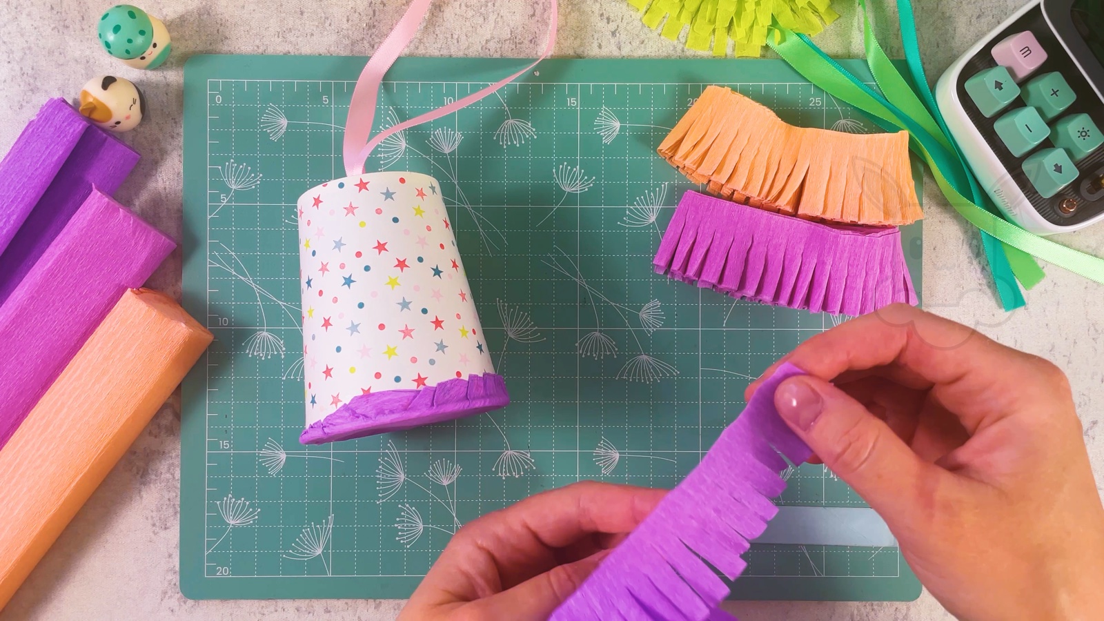 The first purple fringe layer glued around the wide end of the cup, with more fringe strips ready on the mat