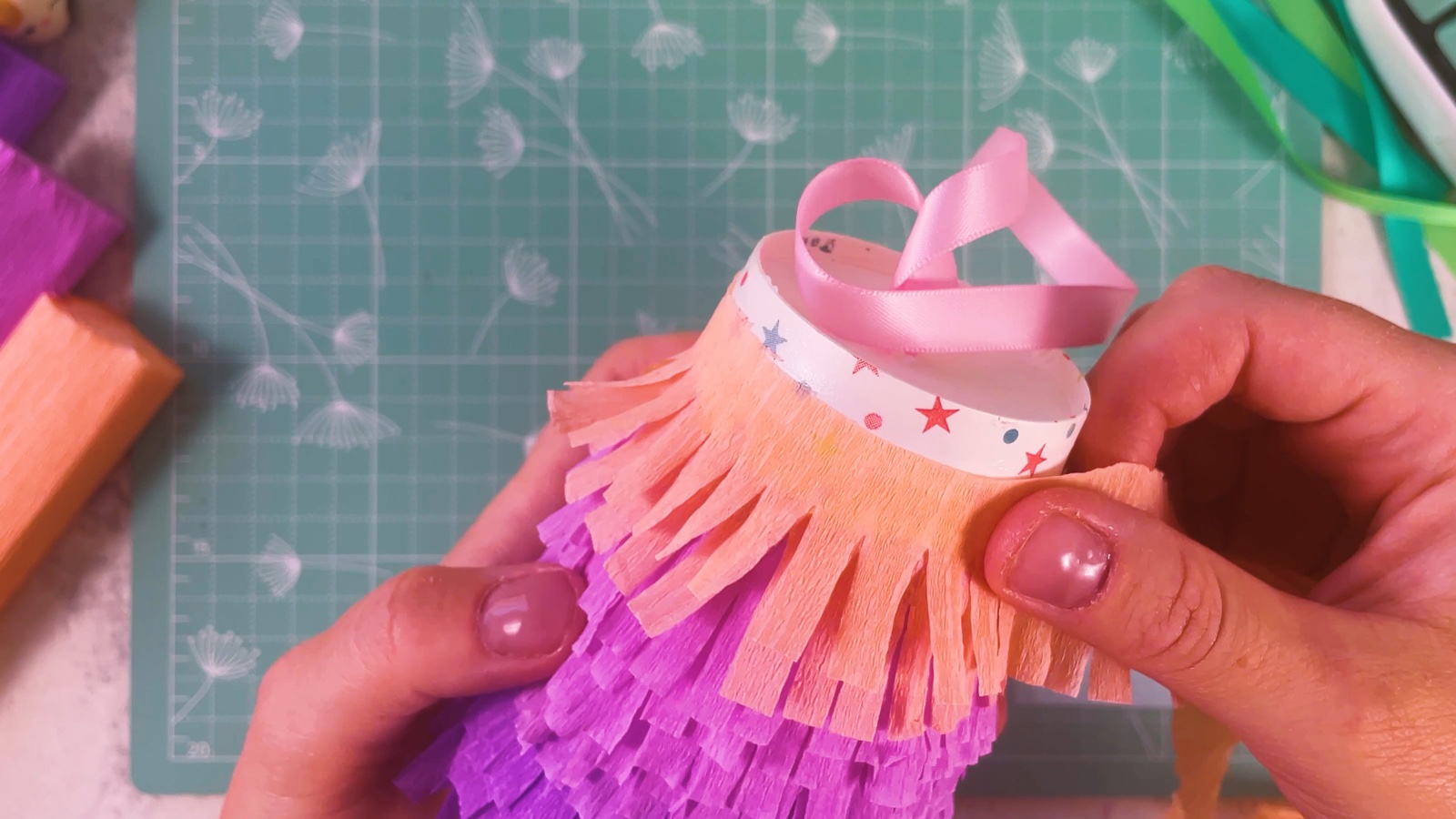 Wrapping the last peach fringe layer around the top of the cup, above the purple and pink layers