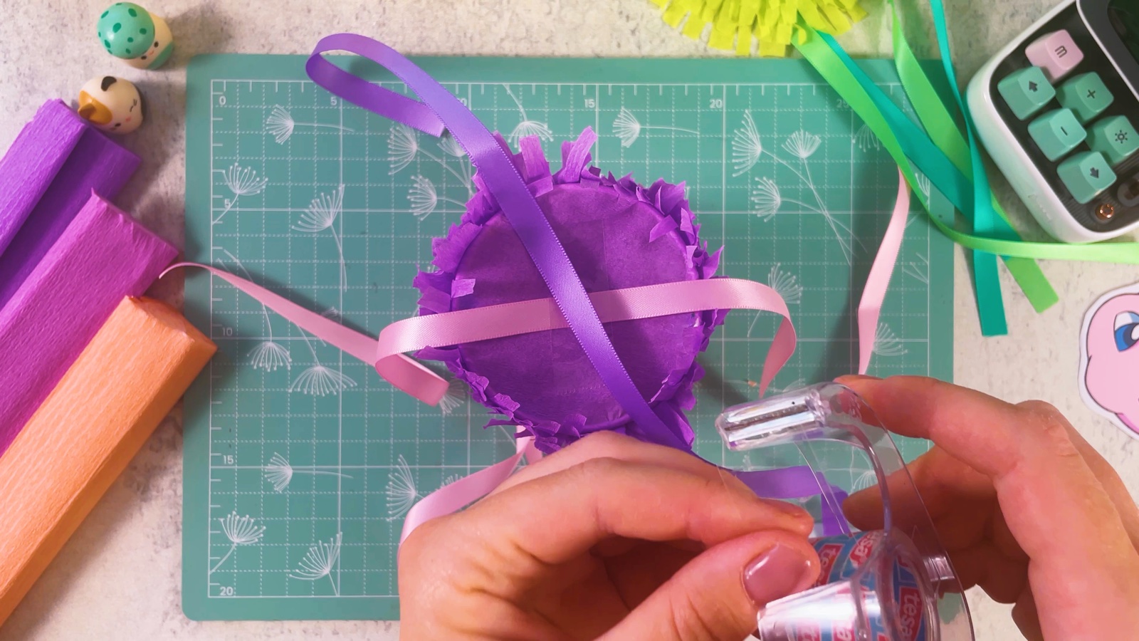 Taping pink and purple ribbons across the paper circle on the bottom of the piñata