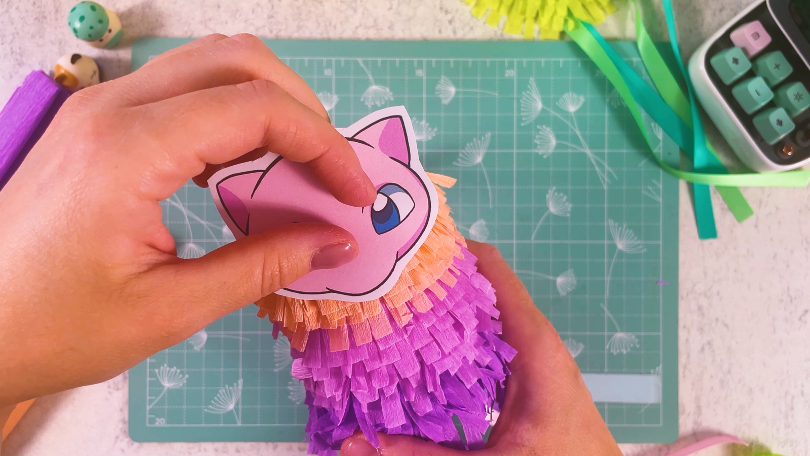 Pressing the printed Mew face onto the top of the fringed piñata