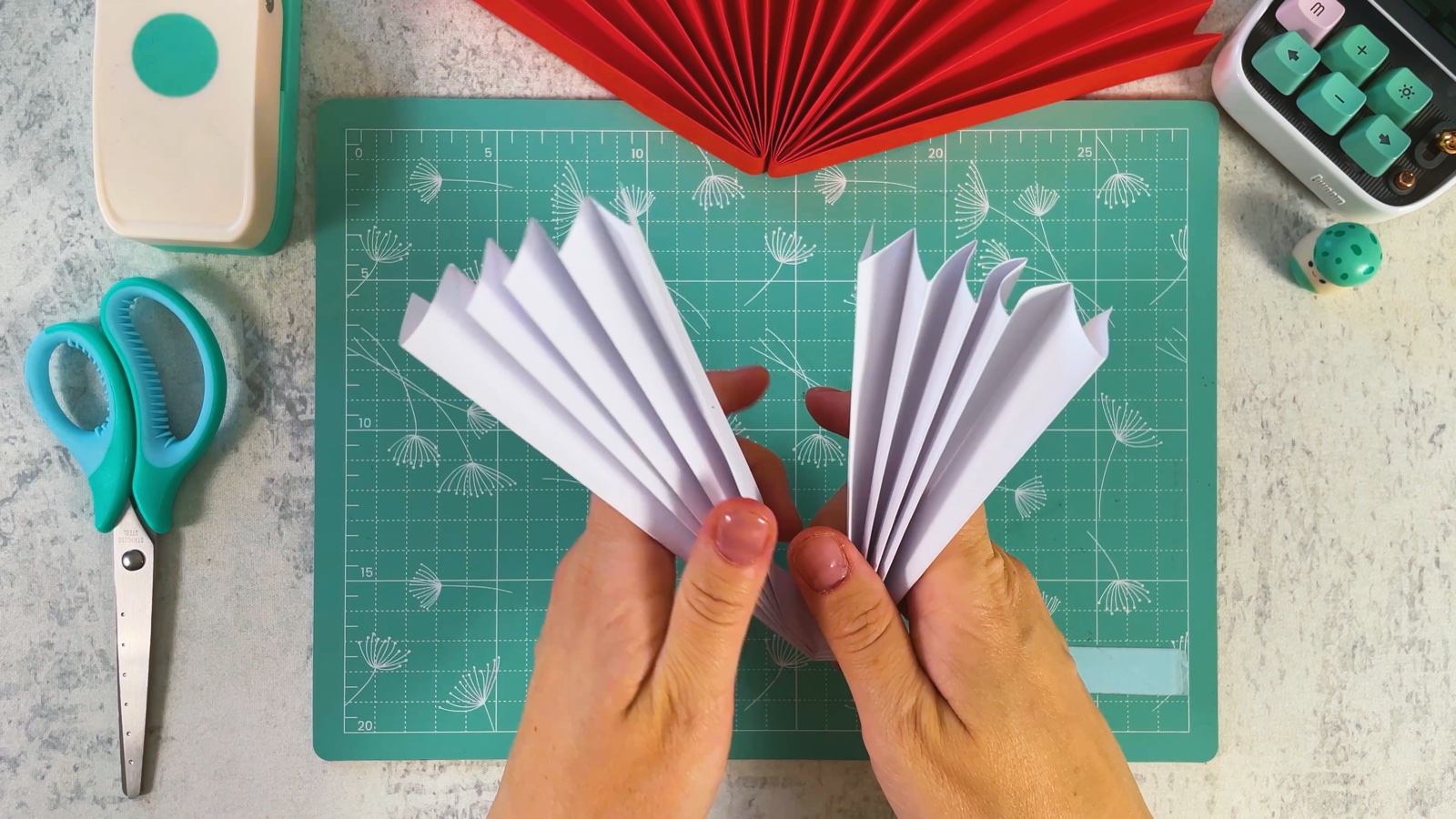 Dos abanicos de papel blanco sostenidos uno al lado del otro, con el medio círculo rojo arriba