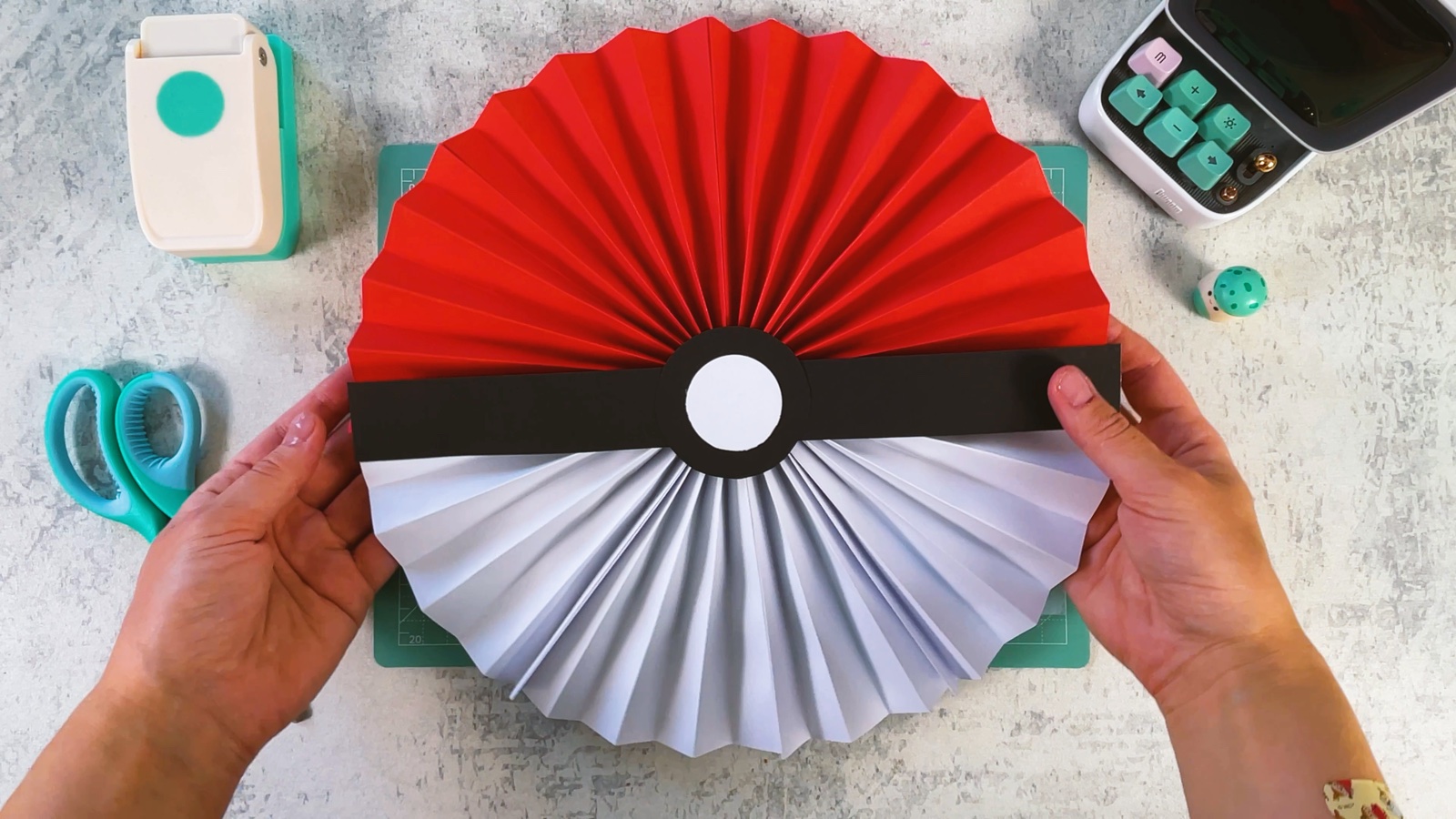 La roseta Poké Ball terminada, roja arriba y blanca abajo, con una franja negra y un botón blanco en el centro