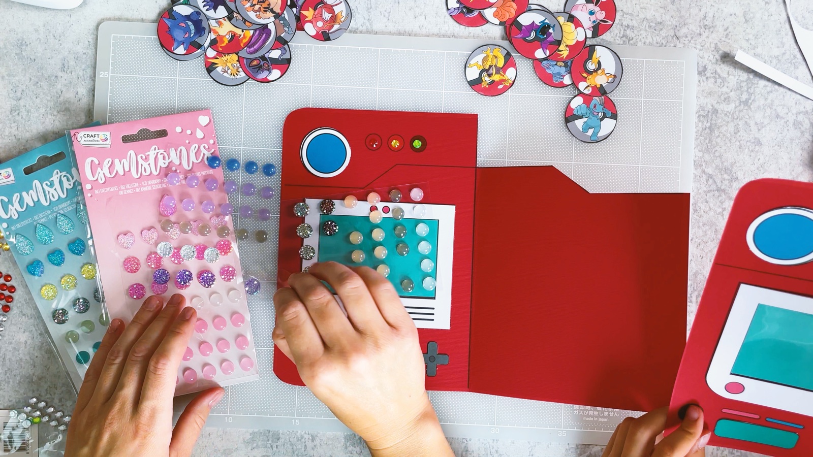 Sosteniendo una hoja de calcomanías de gemas sobre el Pokédex, con las tres luces ya brillando