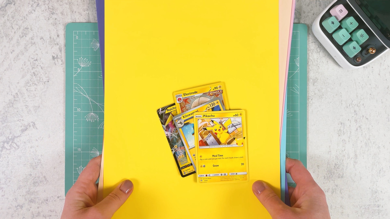 Pikachu and other Electric Pokémon cards on a sheet of yellow paper, with more coloured sheets underneath