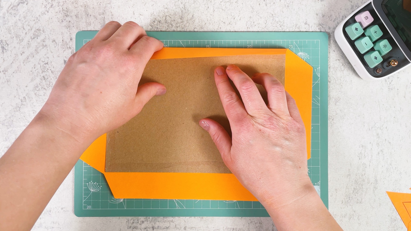 Folding the orange paper edges over the cardboard