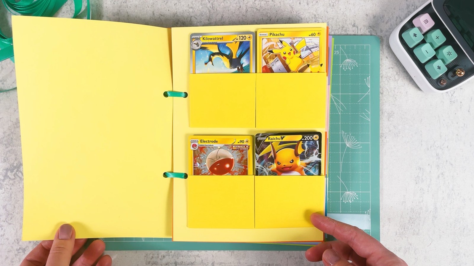 The finished paper binder open on the Electric section, with four cards in yellow pockets and mint ribbons through the holes