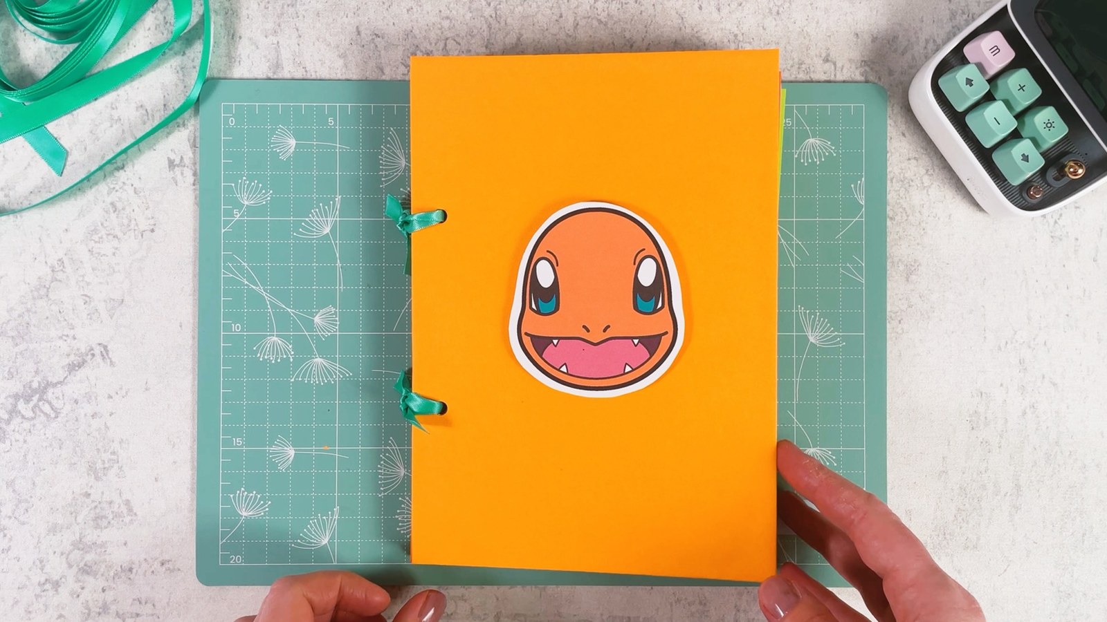 The finished binder closed, with Charmander on the orange cover and two mint ribbon bows along the left edge