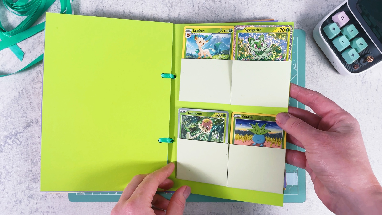 The binder open on the lime green Grass section, with Leafeon, Sprigatito, Toedscool and Oddish cards in pale green pockets