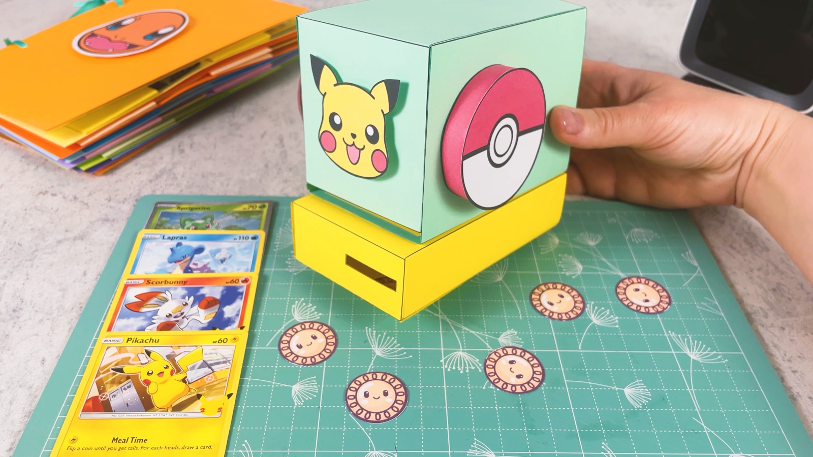 The finished machine: a mint box with a Pikachu face and a Poké Ball handle on a yellow base, Pokémon cards and coins around it