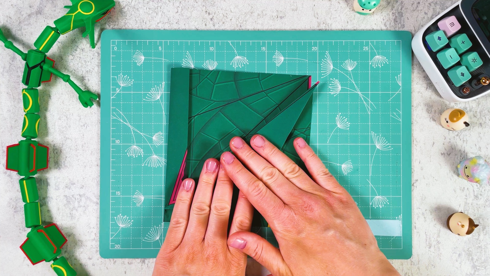 Pressing the second diagonal fold flat, with a thin pink edge showing on the left