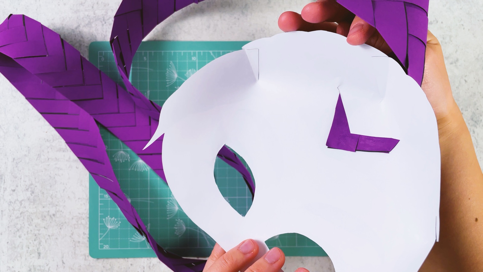 Le dos blanc du masque, avec le bout pointu violet de la tresse collé à plat en forme de V