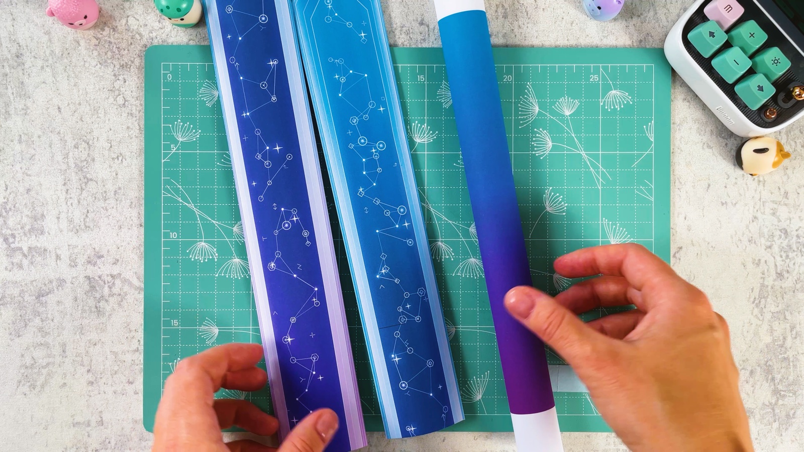 Les morceaux de lame violet et bleu terminés, posés sur le tapis de découpe à côté d’un tube de papier roulé