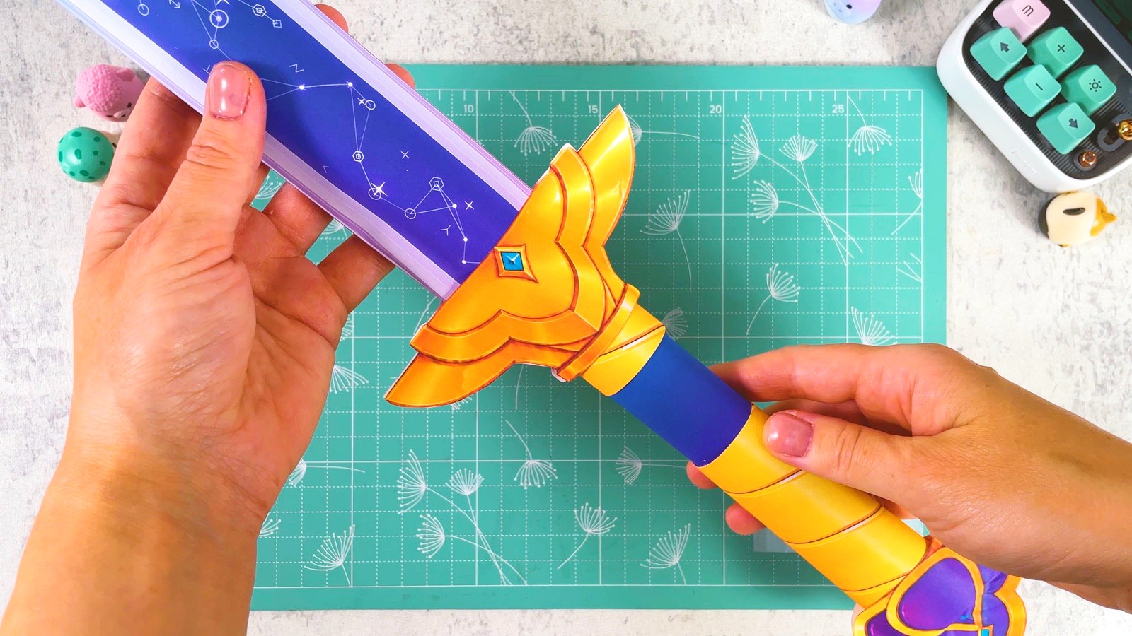 The gold guard and blue and gold handle of the finished paper Rumi sword, held over a mint cutting mat