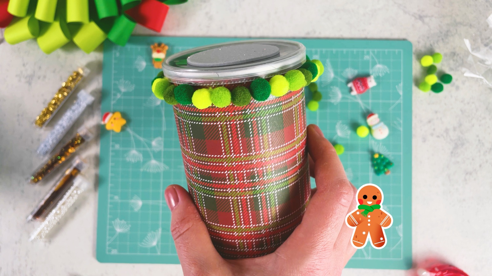 The plaid can with a full ring of light and dark green pom-poms around the top